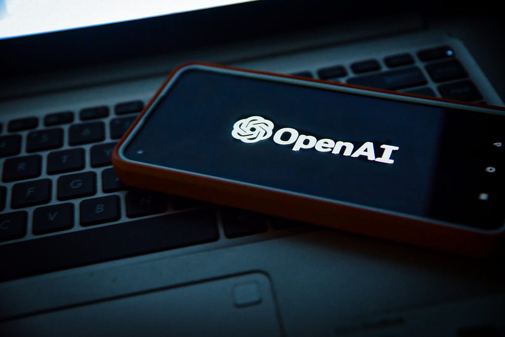 Phone with black background and OpenAI logo sitting on keyboard of laptop