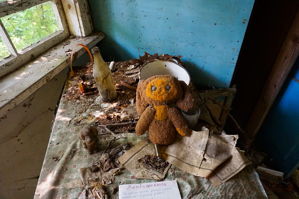 A dilapidated scene with frayed pieces of literature, and empty wine bottle and a cute stuffed animal.