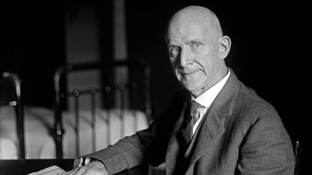 A black and white photo of Eugene Debs, a bald white man in a suit and tie looking at the camera.