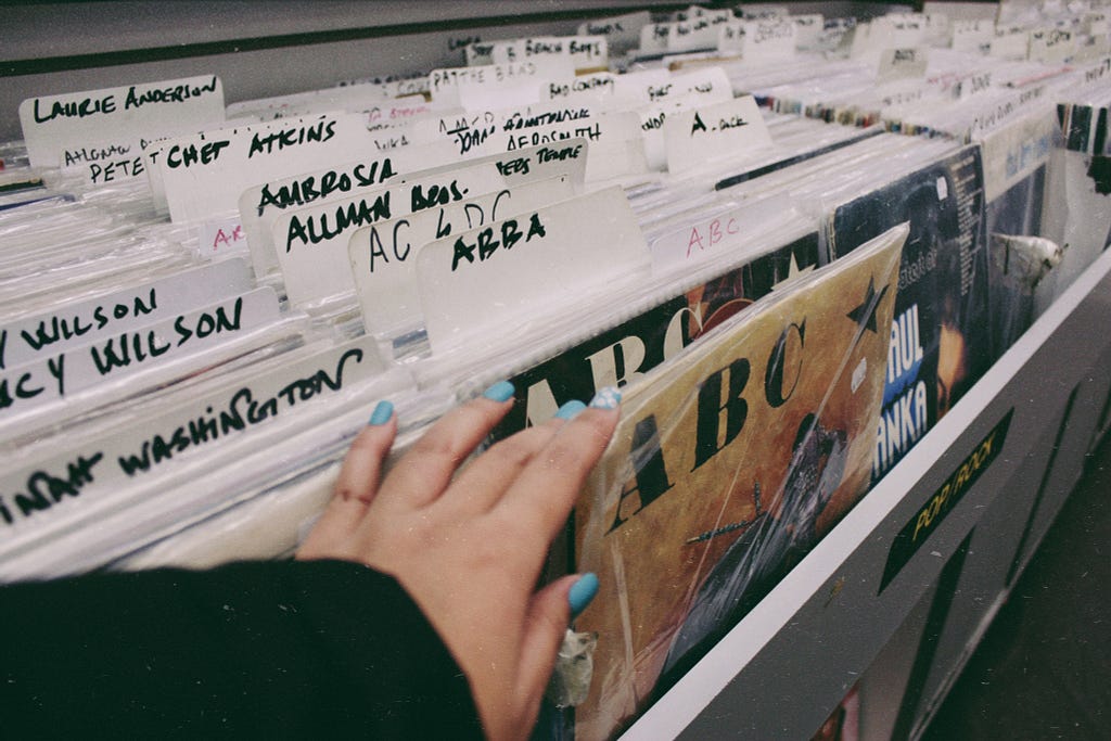 Vinyl records filed alphabetically, someone’s hand is picking out a record titled ABC.