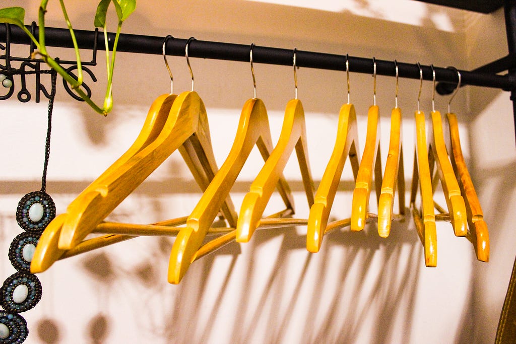 A picture of empty brown wodden hangers in a closet, used to depict one’s closet after decluttering.