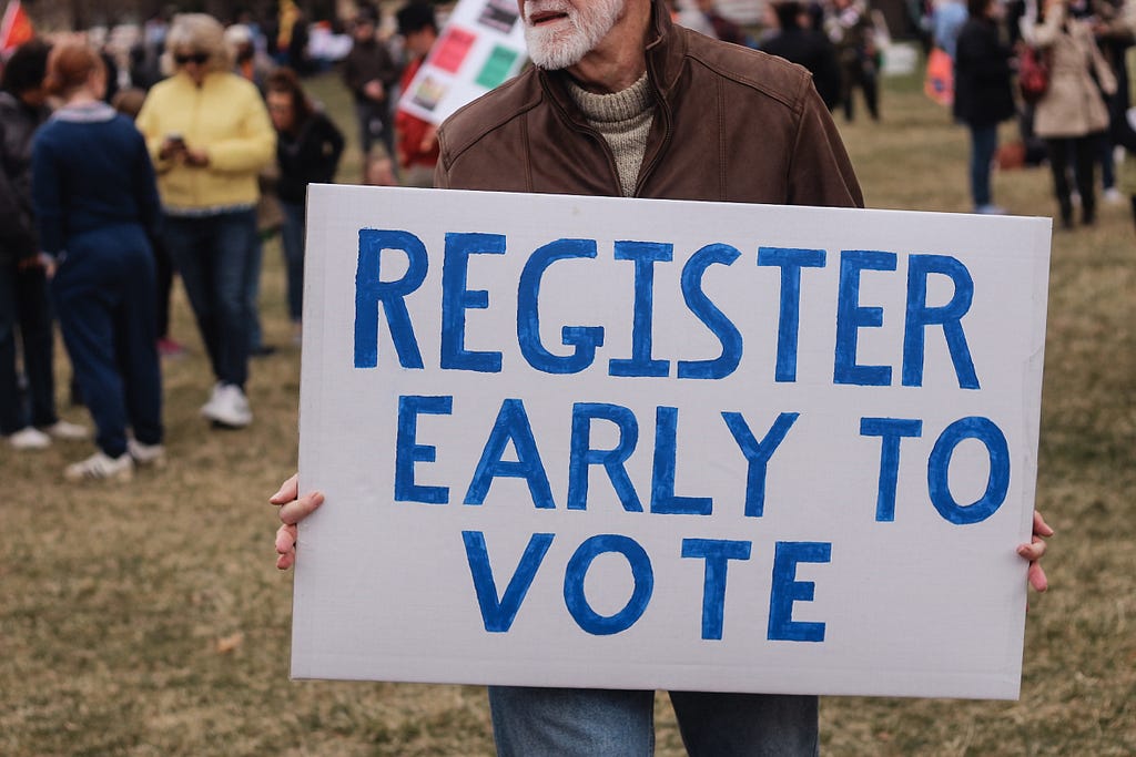 Man holding a sign that says “Register early to vote”