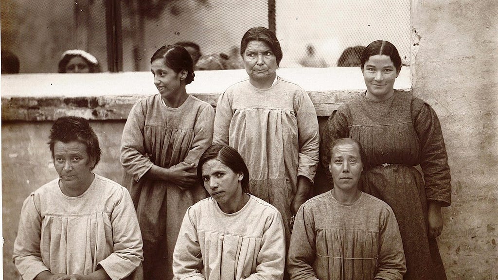 foto di 6 donne rinchiuse in manicomio nei primi anni del 1900. Indossano larghe camicie da notte bianche o grigie.