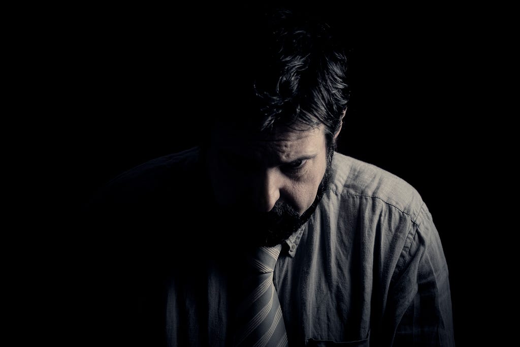 A middle aged man in a grey shirt looking down in depression