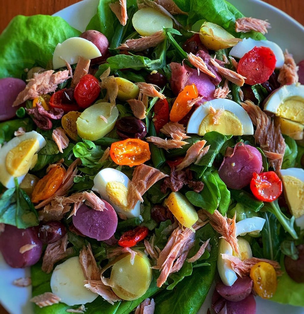 A plate piled high with a vibrant salad containing ingredients like sliced boiled eggs, cherry tomatoes, and shreds of meat.