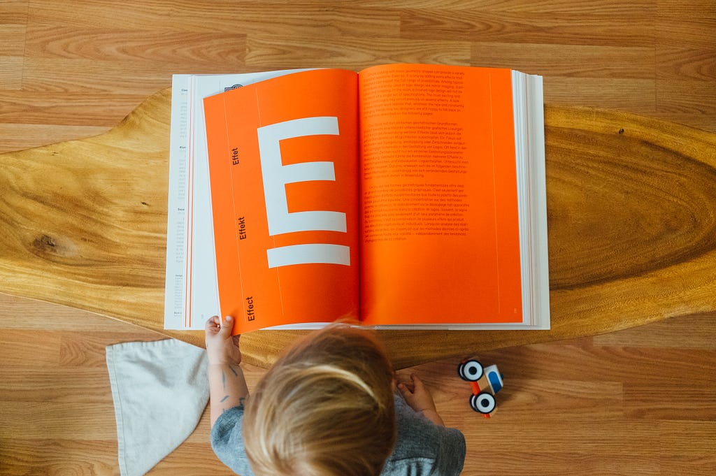 child looking at a book showing a large letter E on an orange background