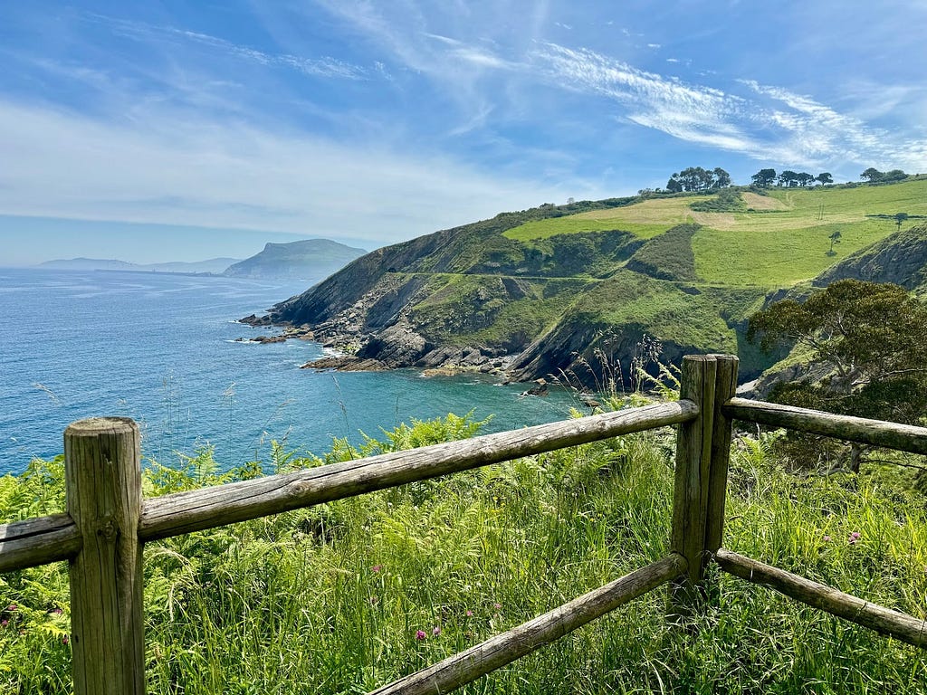 Scenic view of the Spanish hills overlooking the Bay of Biscay with a wooden fence and green vegetation in the foreground.