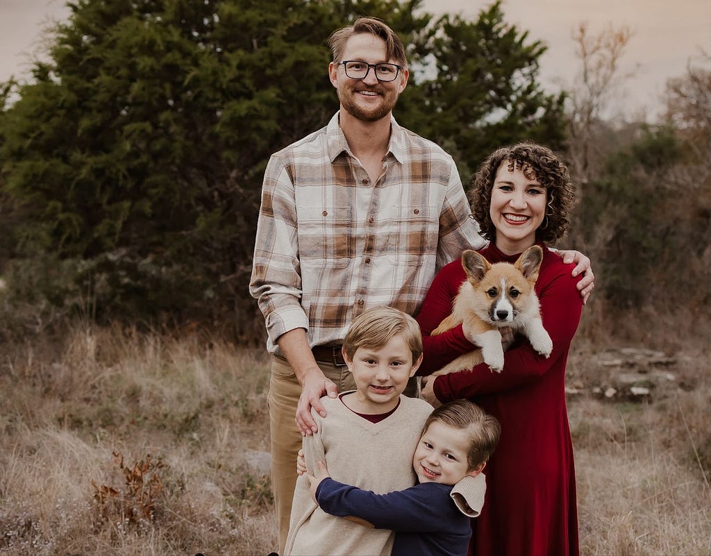 Husband and wife standing outside with their corgi dog and two sons