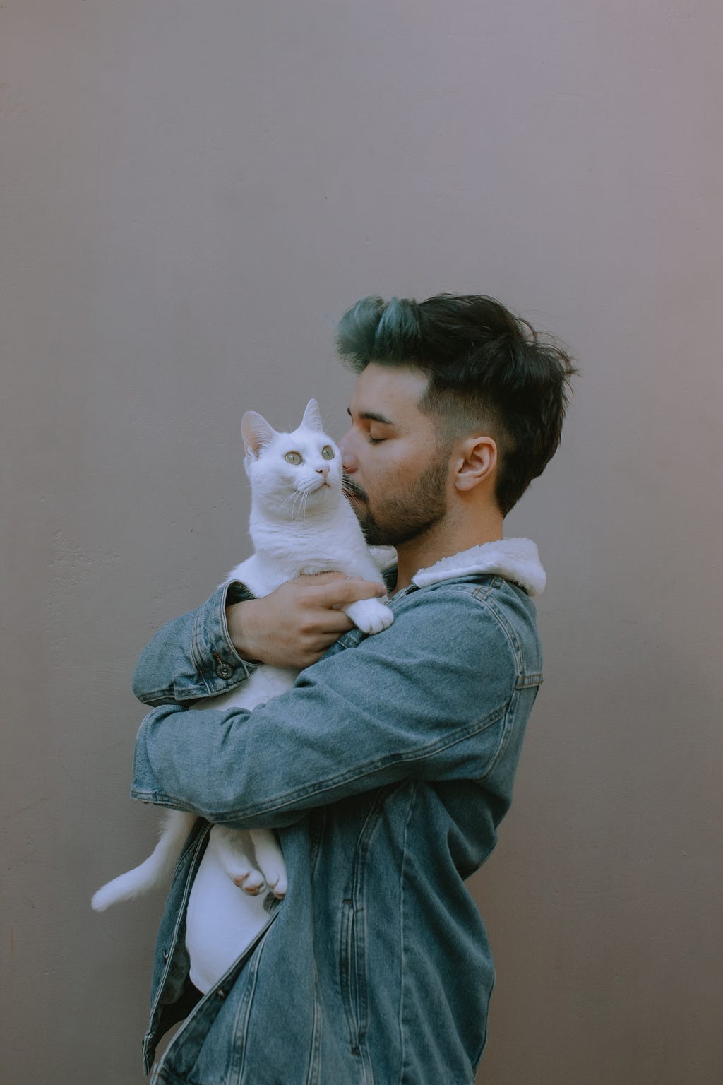 A person with a jean jacket and a beard hugging a white cat