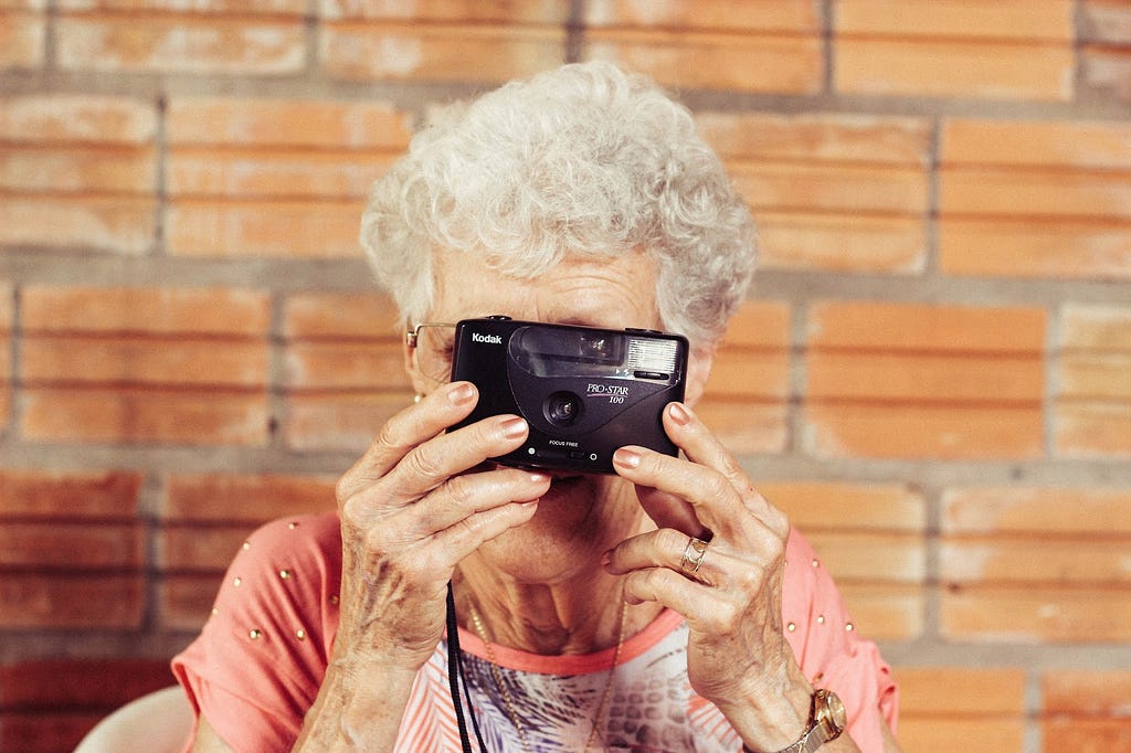 Grey haired woman looking through an analogue camera