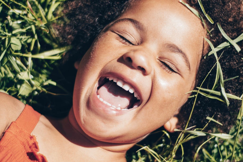 Child laughing with mouth open, lying on the grass. A close up of her face
