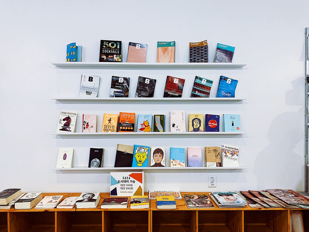 A wall mounted bookshelf featuring 4 shelves with 6 books on each. Minimalist and colorful.