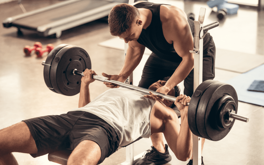 man being spotted while bench pressing standard barbell