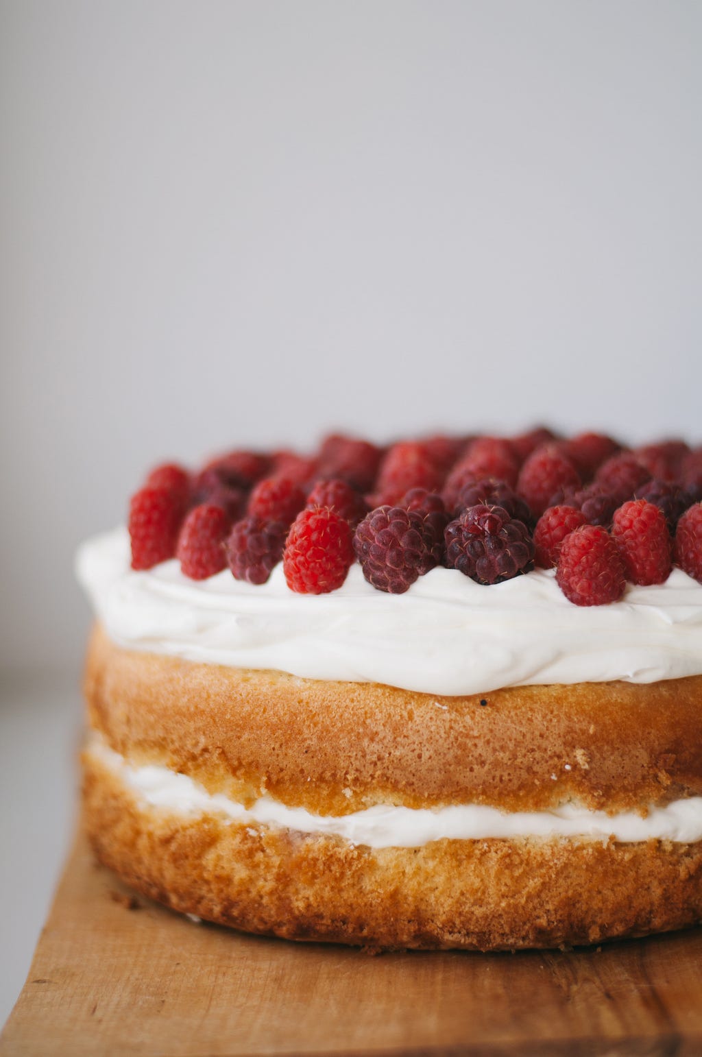 Layer cake with white icing and red raspberries on top. Grey background
