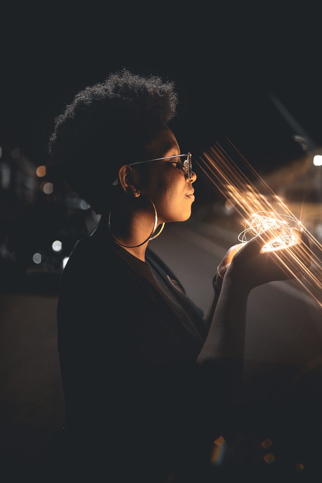 A young woman standing in the dark, holding within her hands, a ball of light.