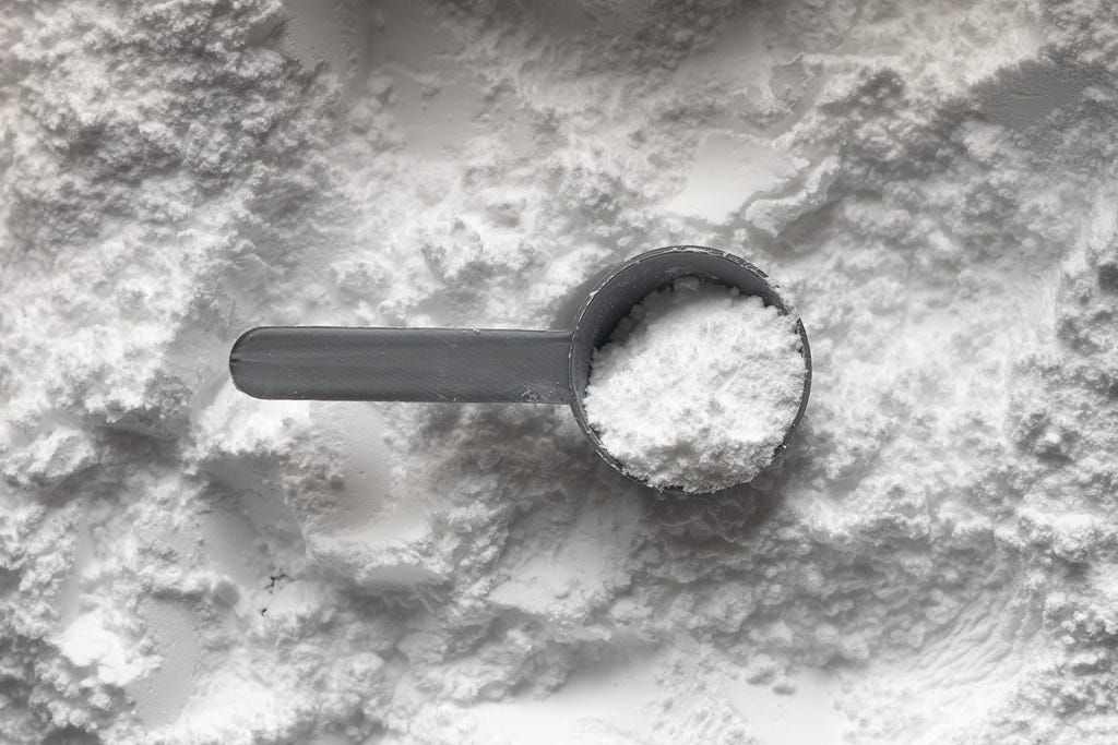 A plastic scoop sits on a pile of powdered creatine