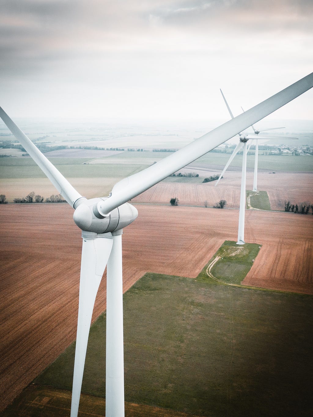 3 wind turbines loom over brown and green fields