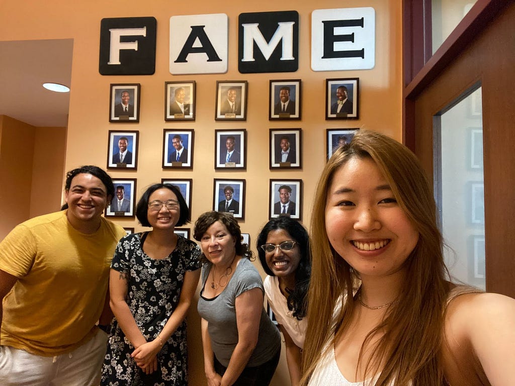 A selfie of the CMU Design team and Marion from FAME in front of The Kiski School FAME photo wall.