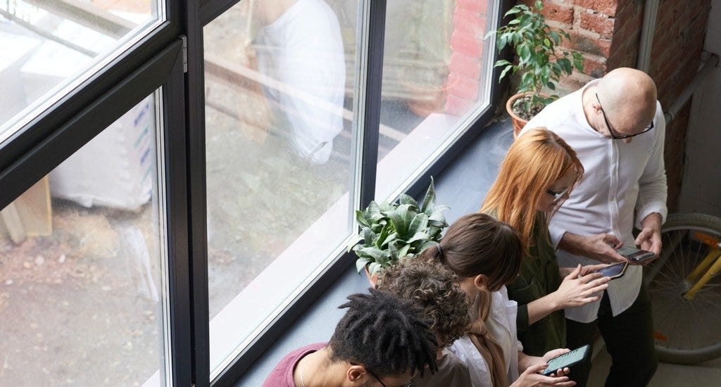 A group of people using their smart phones while standing next to each other