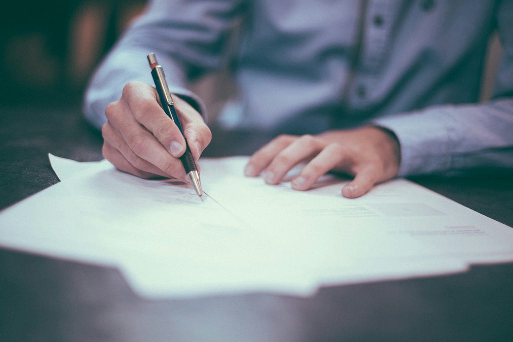 A man sits at a desk and scans through permit papers with a black pen.