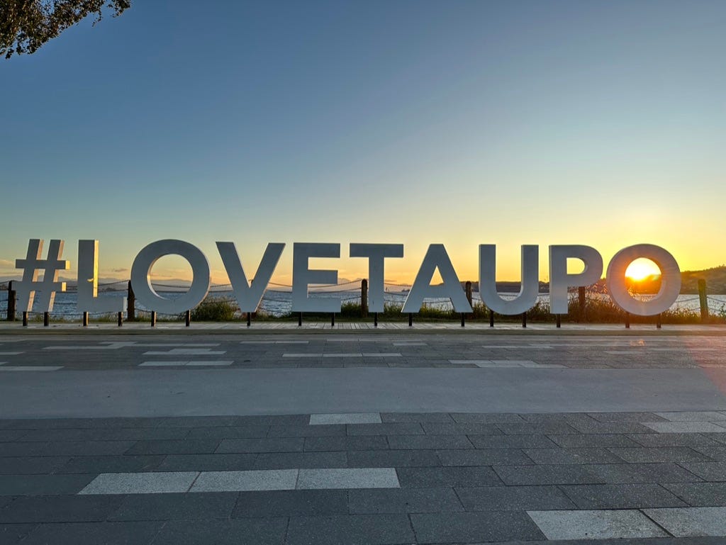 #LOVETAUPO sign on road with sunset and sun centred in the middle of the “O.”