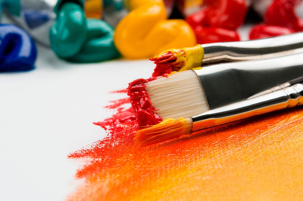 Close up of brushes on a canvas covered in red and yellow paint 