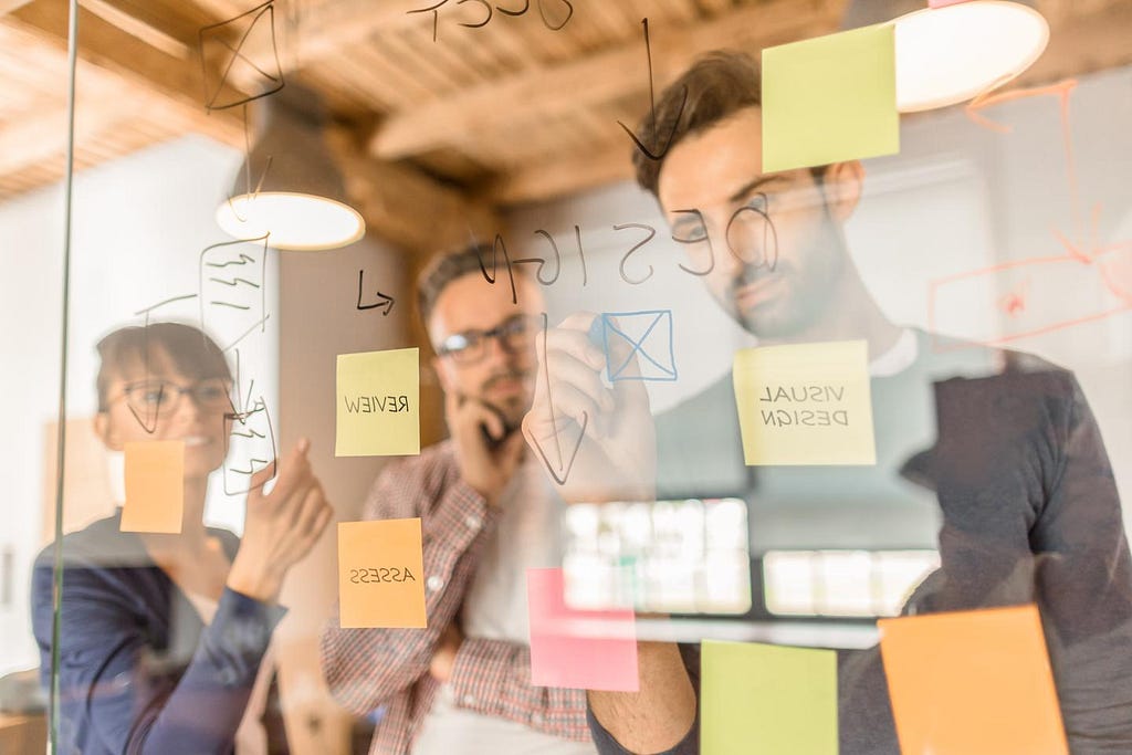 A team of 3 people working out a design schema on a transparent glass board