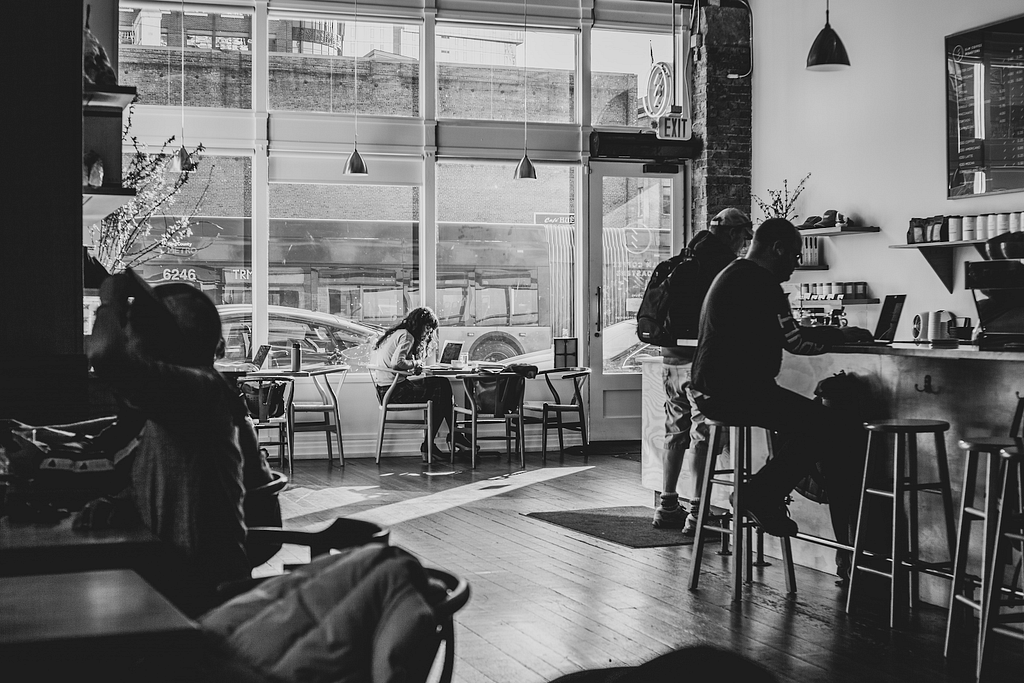 A black and white photo of people in a café with glass windows.