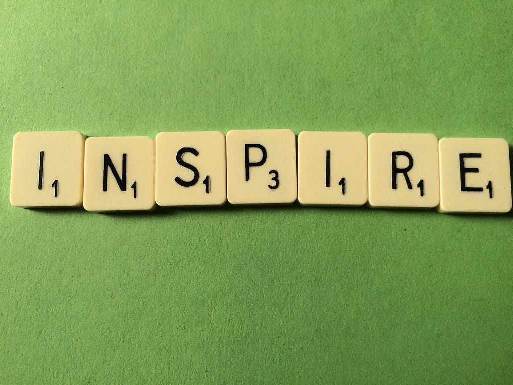 Peças do jogo palavra cruzada dispostas sob uma superfície verde, formando a palavra "inspire"