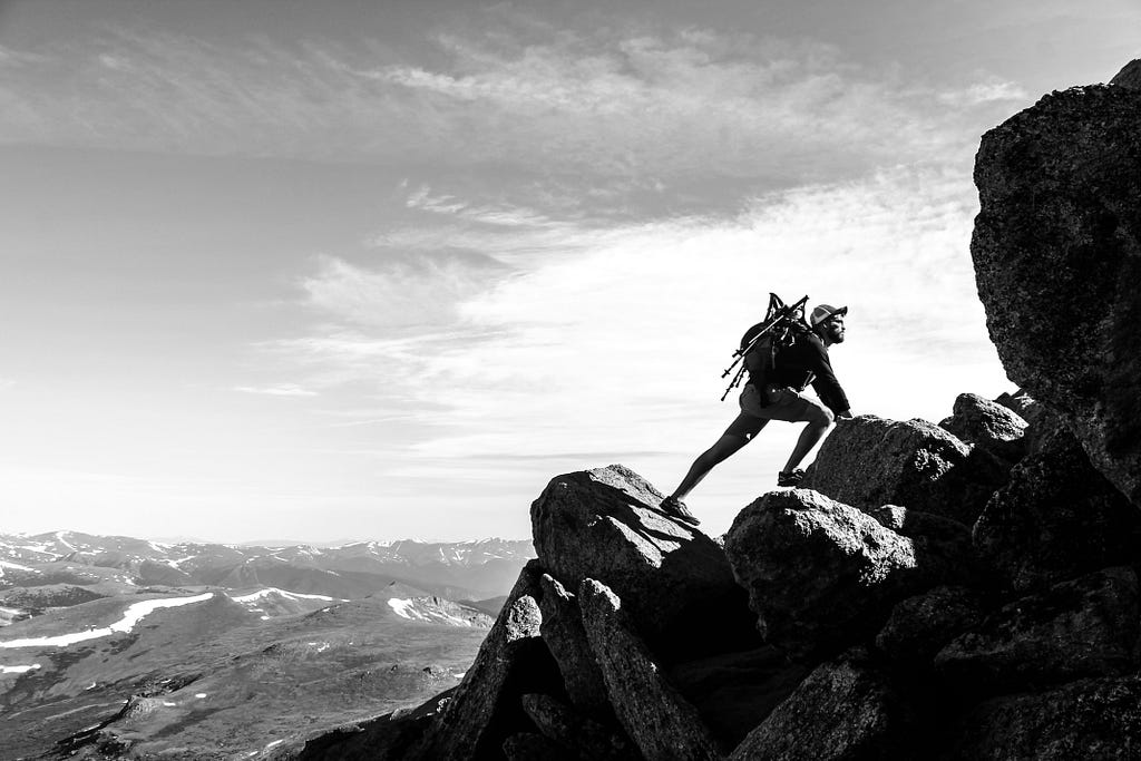 A black and white side profile image of a man climbing a mountain.