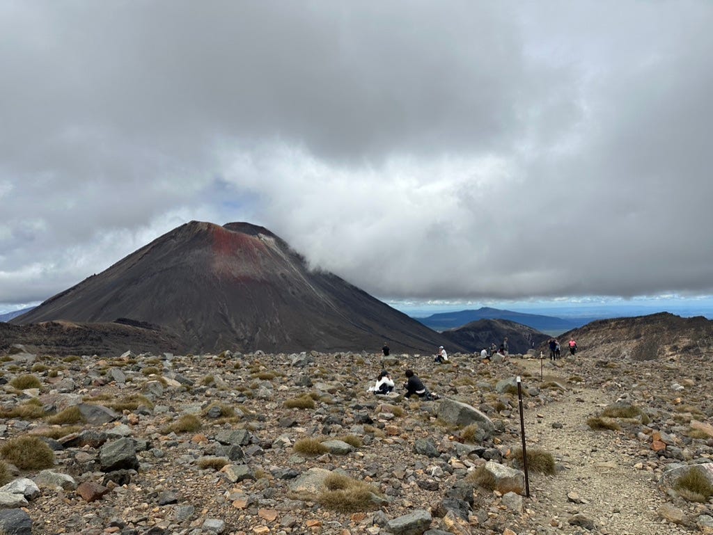 View of volcano with rocks in foreground and people dotted around.