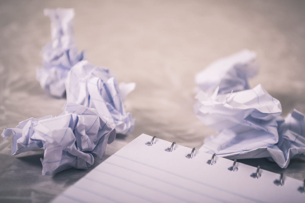 Image of a notepad with a blank page and crumpled balls of paper around it.