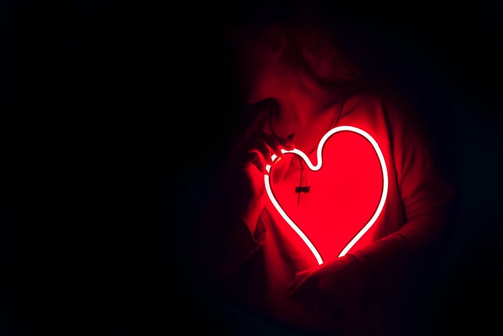 A woman holding a red neon heart in a dark room