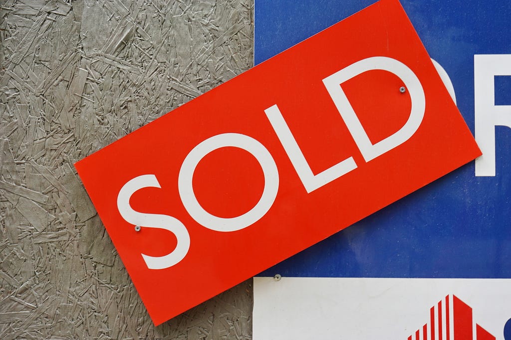 Picture of a sold sign on top of a real estate for sale board.