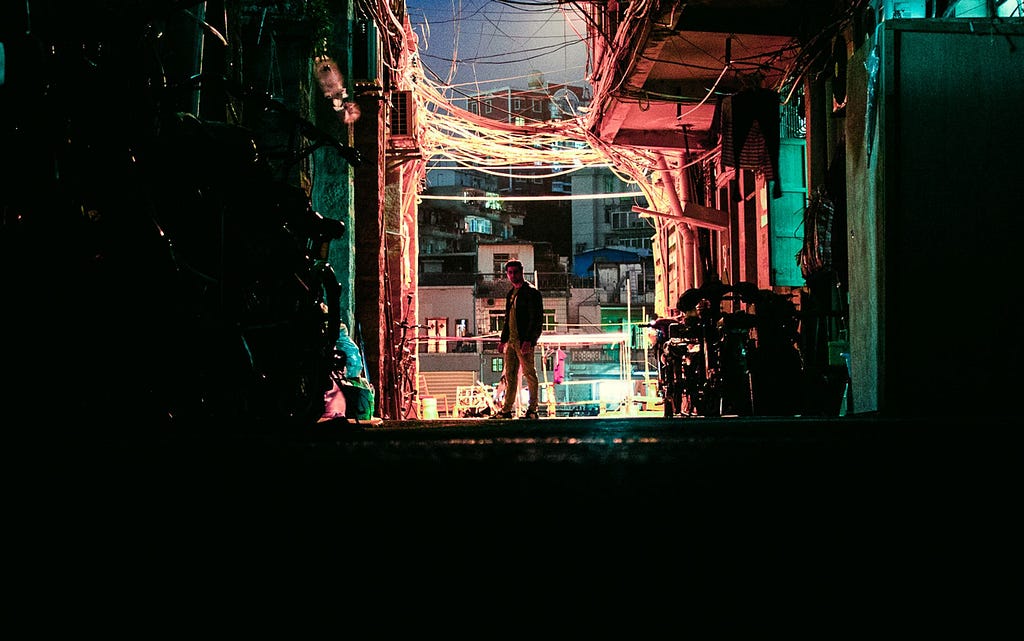 Man standing in the middle of a dark alley with green and orange lights
