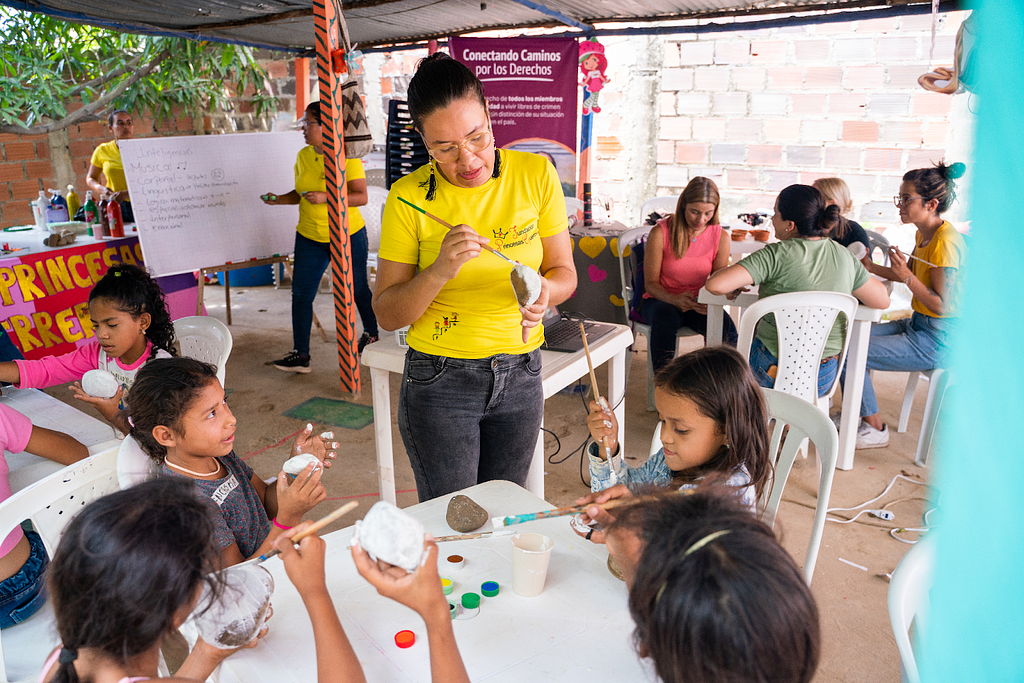 A woman leads girls in a rock painting activity.