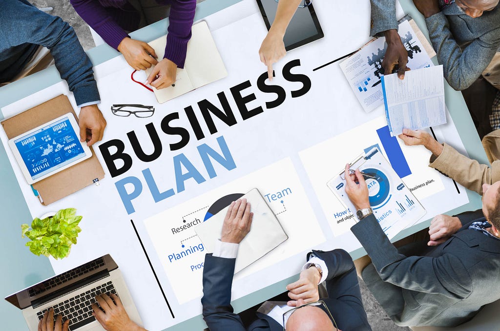 group of people sitting around a table with “business plan” written on it