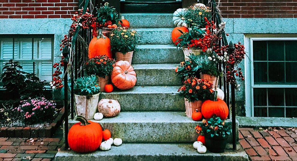 The outdoor front stairs of a house decorated with natural leaves and pumpkins