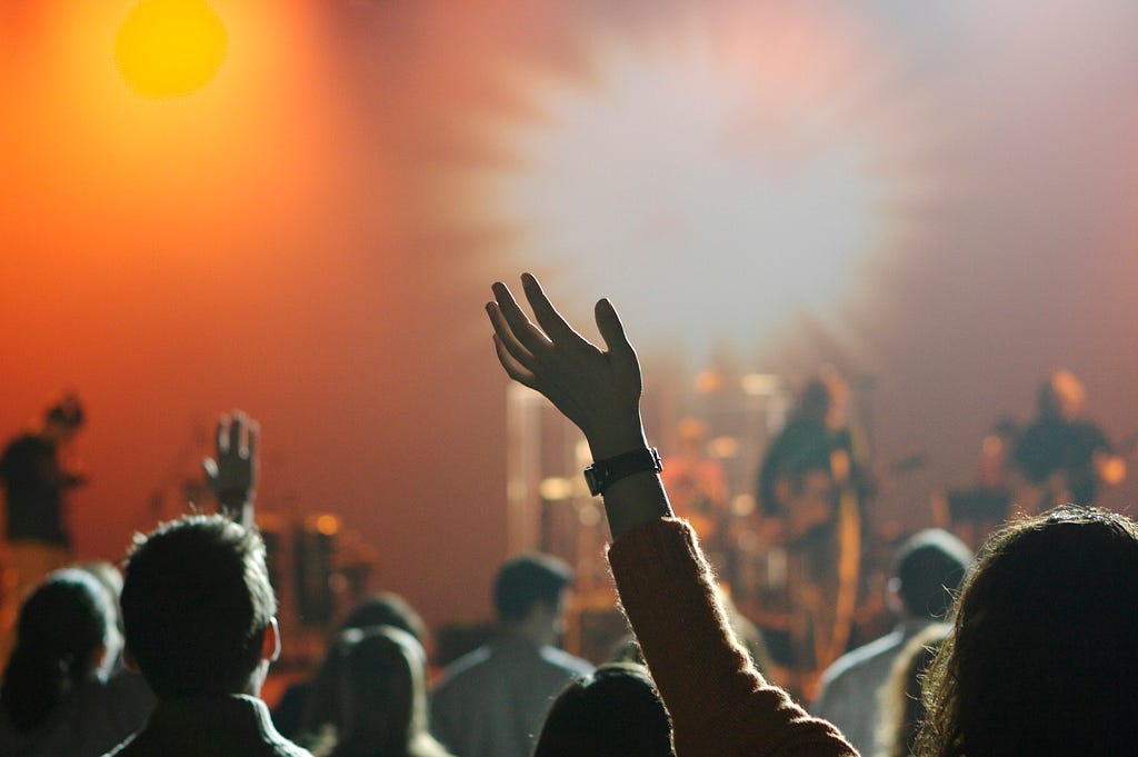 People excitedly cheering at a concert, band in the background.