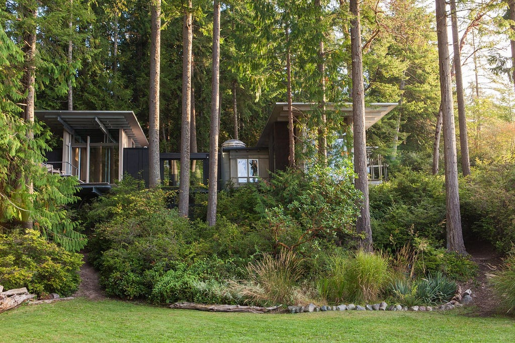 Outdoor, Shrubs, Grass, Woodland, Trees, and Back Yard In the 1980s, the retreat was made up of three tiny pavilions linked by wooden platforms. By 2003, the pavilions had been connected by a unifying roof, creating a single form grounded onto the hillside and projecting out over the landscape.&nbsp;