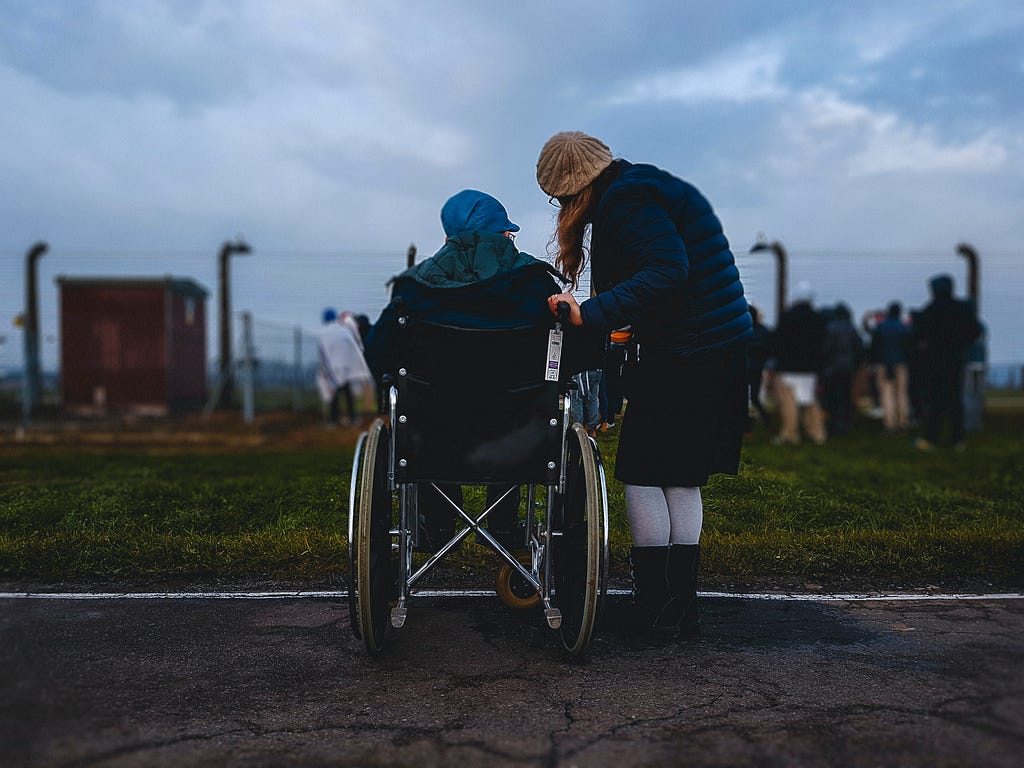 A woman taking her closest (who is in a wheelchair) outside (feeling a sense of warmth, a connection and calmness). They are embracing nature together