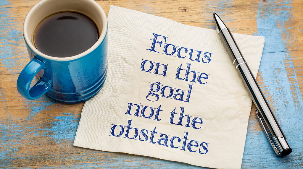 Blue mug, pen, and paper which says “Focus on the goal not the obstacles”