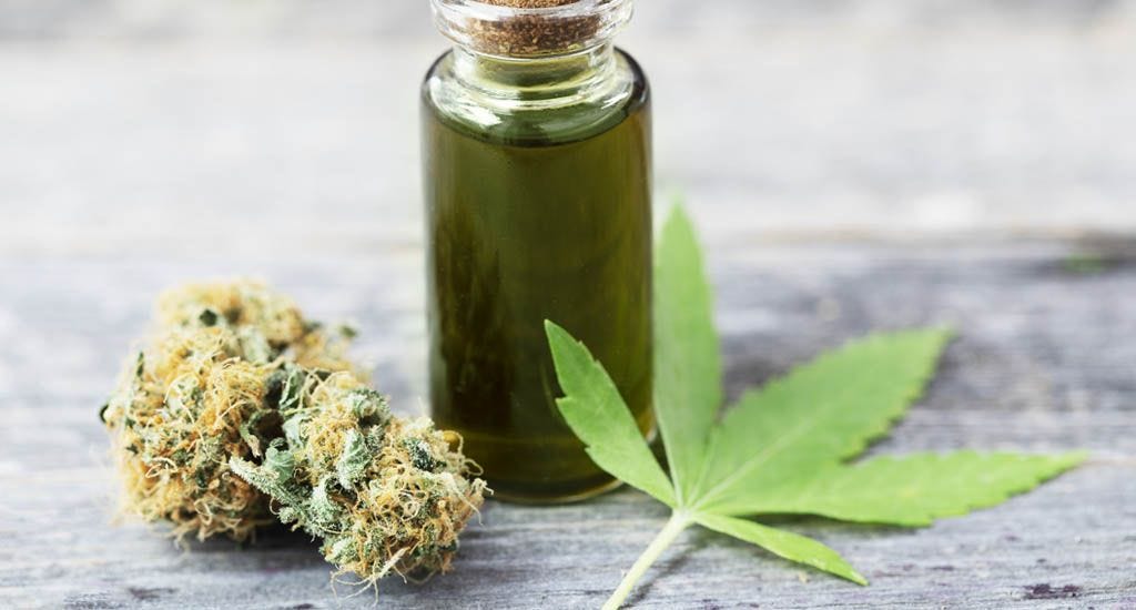 Cannabis oil in a small bottle with bud and leaf on wooden surface