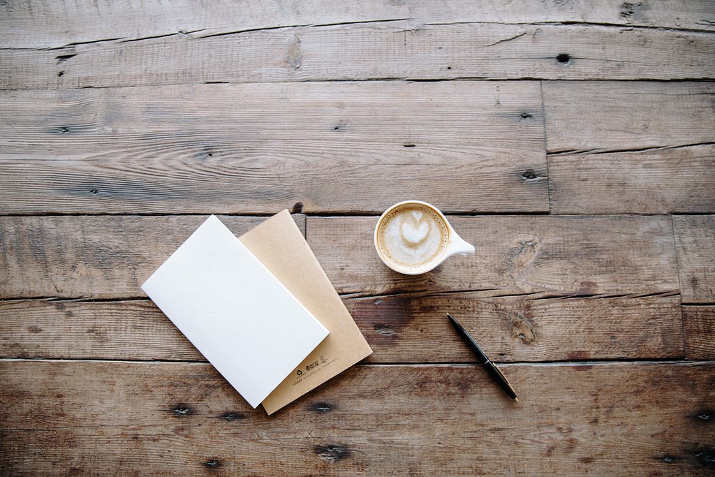An empty notebook, a pen and a cup of coffee