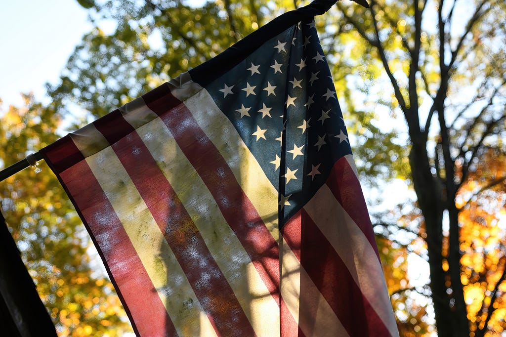 An old American flag hangs in front of a home, lit by a golden sunset. The story that follows is a tribute to a man who served in the United States Navy during World War Two.