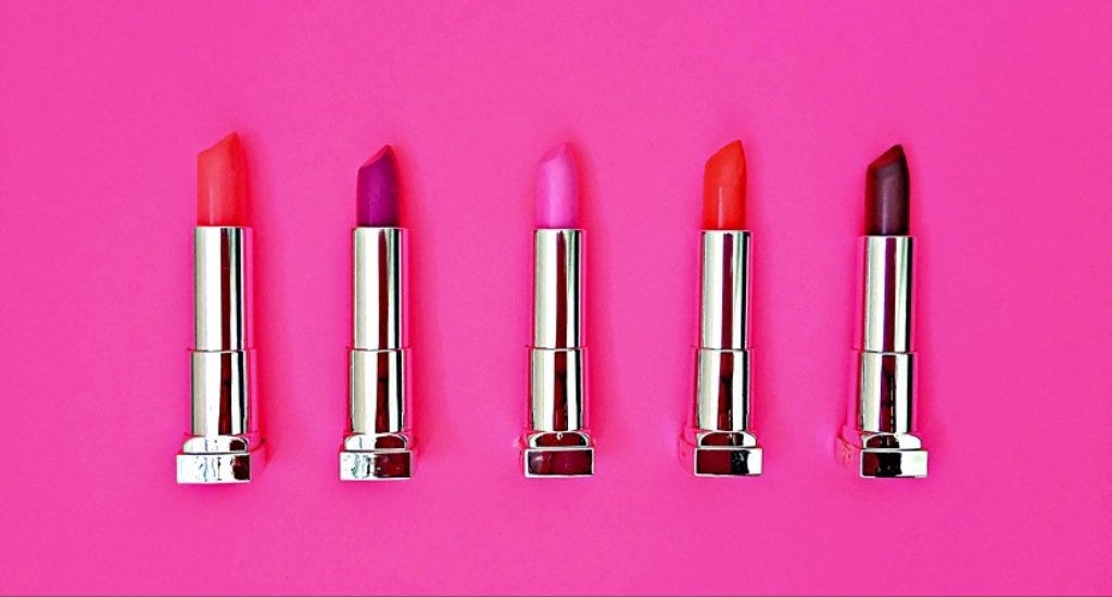 Five tubes of lipstick with a pink background