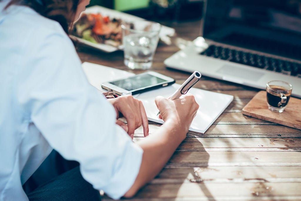 A white woman takes notes on paper in front of her computer