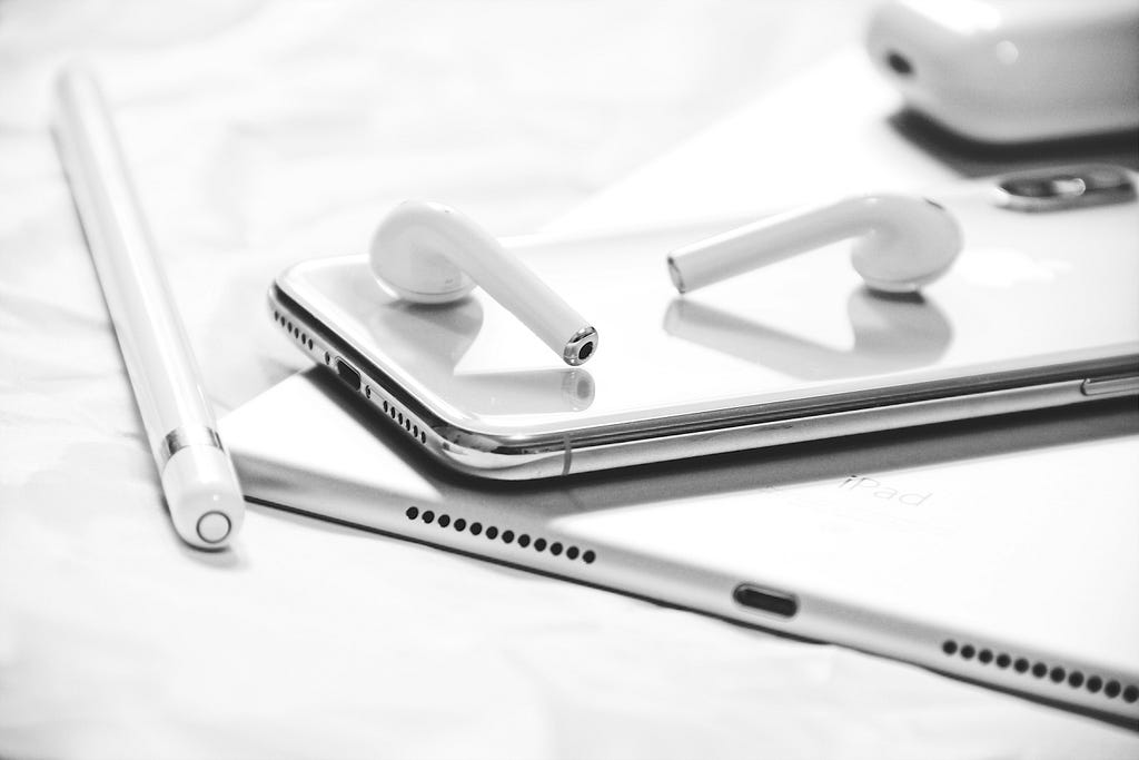 Some sleek, shiny ear buds on top of a smooth, curved phone and tablet.