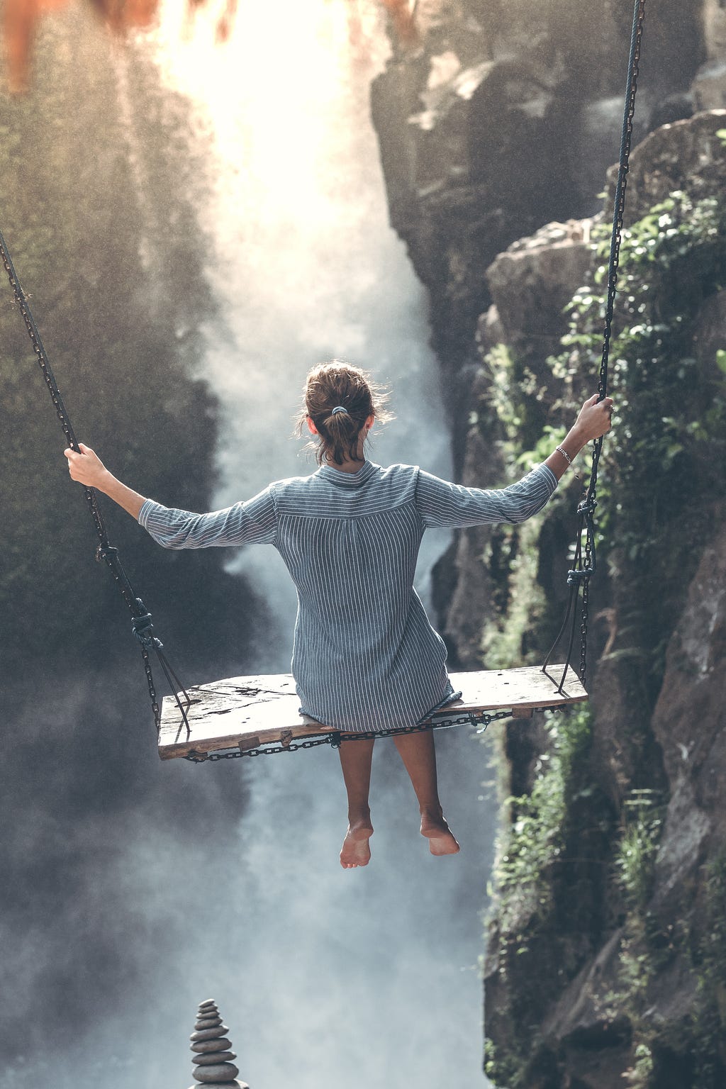 A picture of a lady on a swing swinging forward into a foggy narrow space between two steep cliffs. It signifies a jump into the unknown or murky waters but going anyway