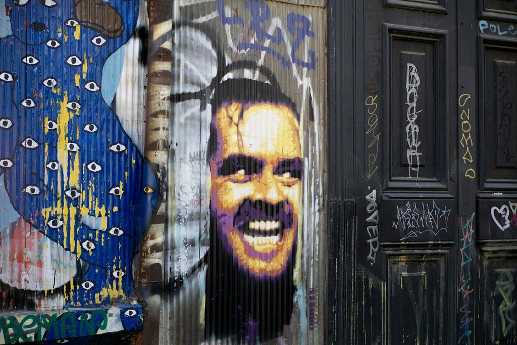 a color collage of street art including a painted blue body with eyes, and a photo realistic image of Jack Nichloson’s “Here’s Johnny” bursting through the door